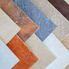 Overlapping rectangular stone or tile samples arranged diagonally, showcasing a range of colors and textures including beige, terracotta, blue-gray, cream, and brown.